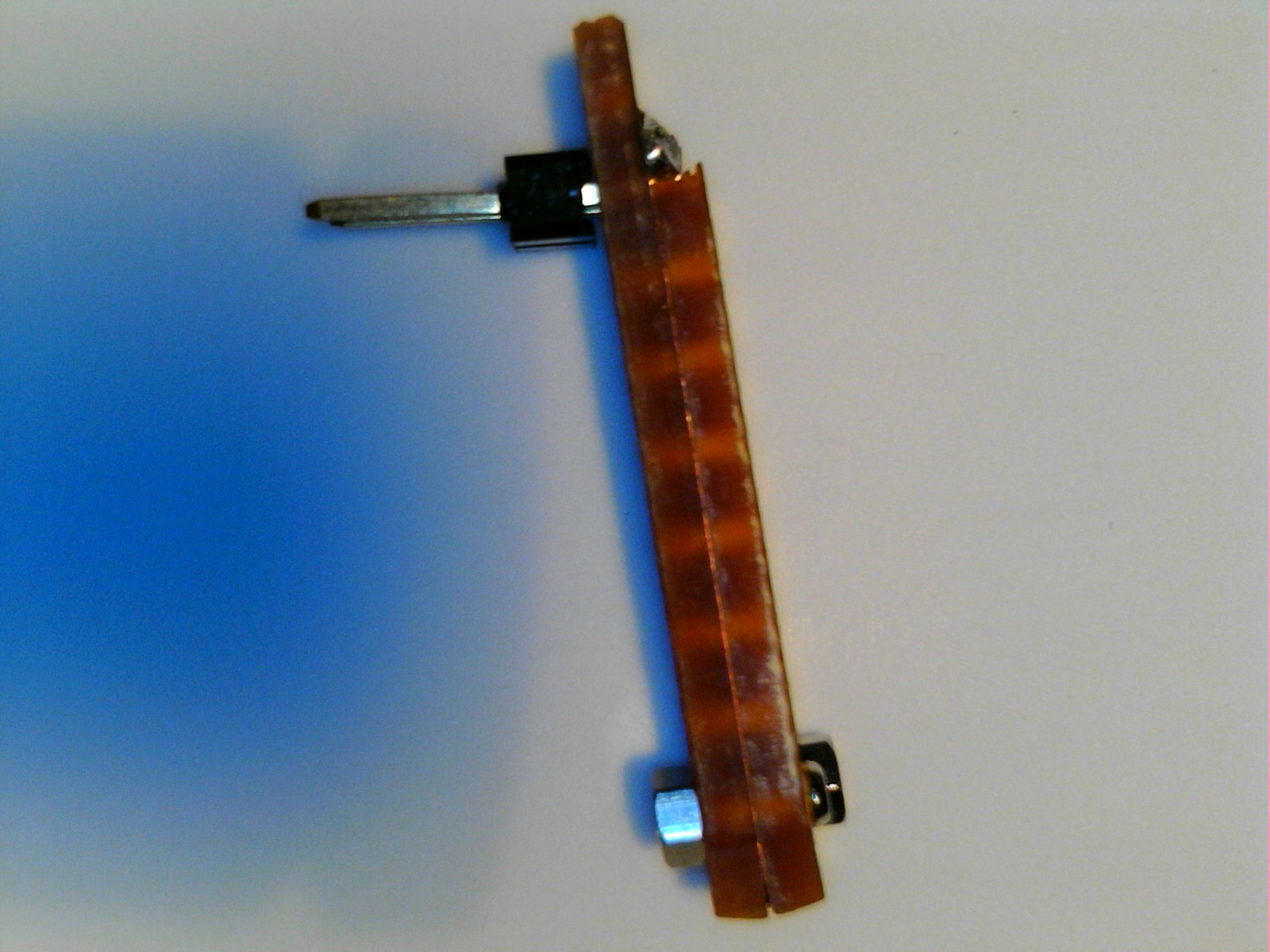 A view of the gen 2 print head from the side showing how the clamp screws go throughthe assembly holding the two piece of strip board together and clamping the filament at the end of the assembly. Also, the variance in height of the strip boards to allow for soldering the header pins in is shown.